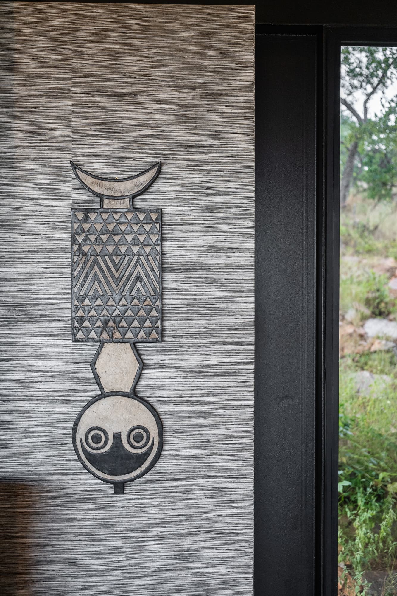 Carved African wooden mask with geometric patterns hanging on a gray textured interior wall.